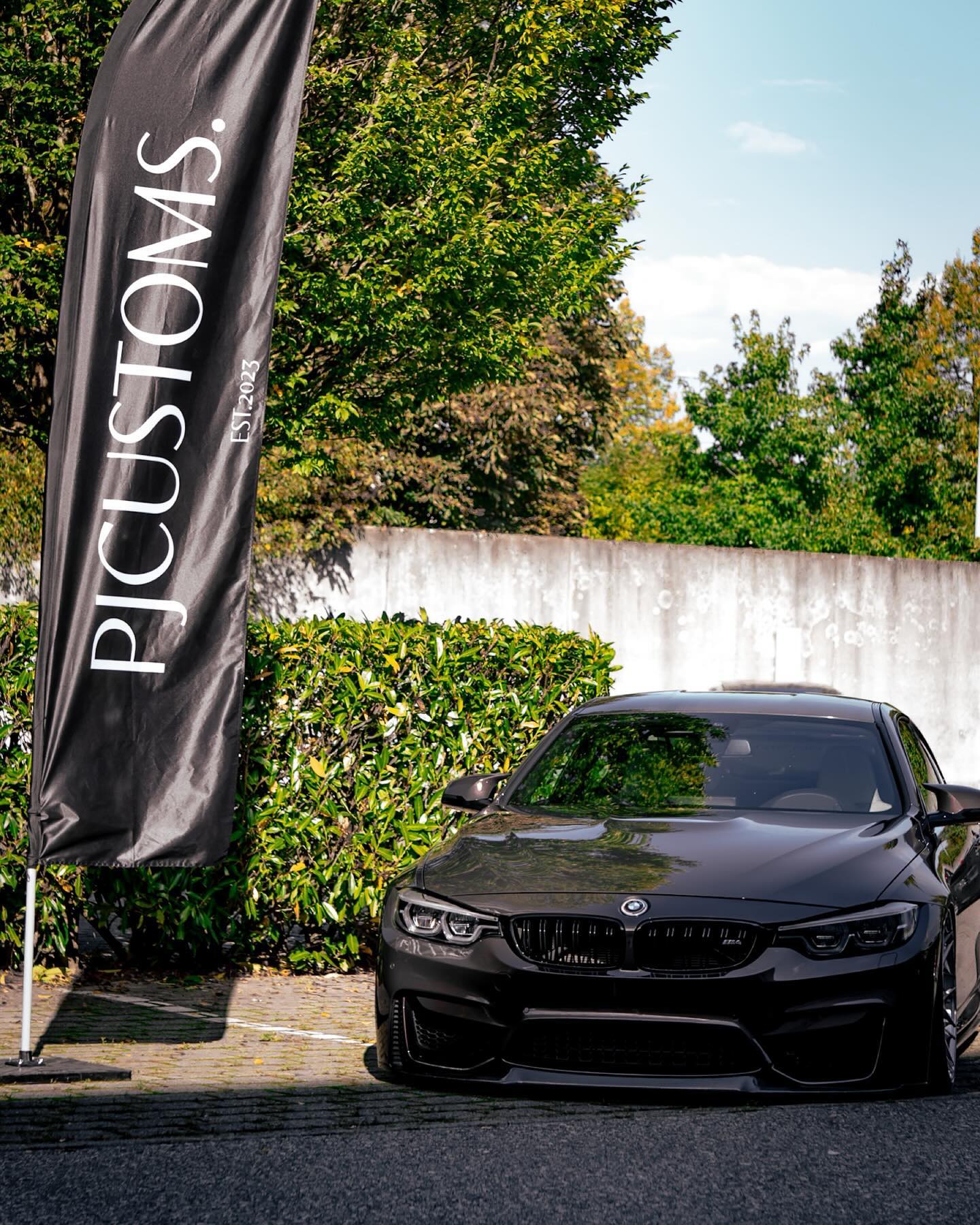 Schwarzer BMW M4 vor der PJ Customs Flagge