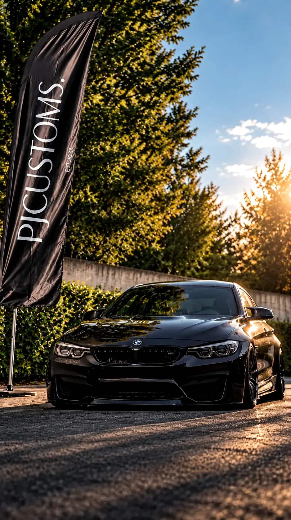 Schwarzer BMW M4 vor der PJ Customs Beachflag auf dem Garagenplatz in Rohrbach, Abendlicht